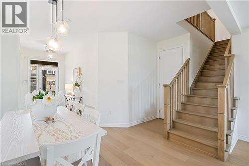 Hardwood flooring, natural wood staircase with balusters, contemporary pendant lighting, and a white paneled door - 68 Barkerville Drive, Whitby, ON 