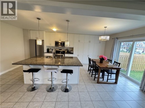 Spacious kitchen featuring an expansive center island with granite-finish countertop, white cabinetry, integrated stainless steel appliances, and tile flooring - 67 Pointer Street, Cambridge, ON 