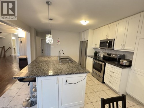 Kitchen featuring a granite-topped island with an undermount sink, white shaker cabinetry, stainless steel appliances, and tile flooring - 67 Pointer Street, Cambridge, ON 