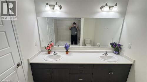 Double vanity with undermount sinks and dark wood-finish cabinetry, illuminated by two wall-mounted light fixtures - 67 Pointer Street, Cambridge, ON 