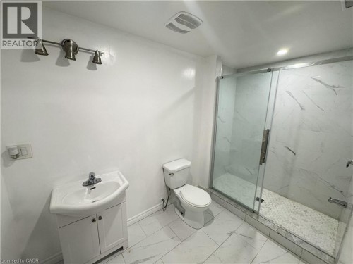 Glass-enclosed shower with white hexagon mosaic tile floor, white patterned wall tile, and a single vanity with a white ceramic sink - 67 Pointer Street, Cambridge, ON 
