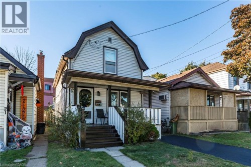 Front exterior featuring light-toned horizontal siding, a covered porch with white railings, and dark wood-finish steps - 23 Frederick Avenue, Hamilton, ON 
