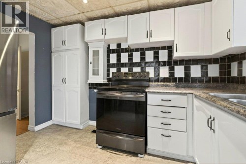 White cabinetry with black hardware, checkered tile backsplash, stainless steel range, and stone-finish countertops - 23 Frederick Avenue, Hamilton, ON 