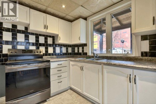 White cabinetry, checkerboard tile backsplash, stainless steel range, and a double basin sink - 23 Frederick Avenue, Hamilton, ON 
