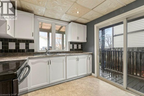 Kitchen featuring white cabinetry, patterned backsplash, light-colored flooring, and a sliding glass door to an outdoor area - 23 Frederick Avenue, Hamilton, ON 