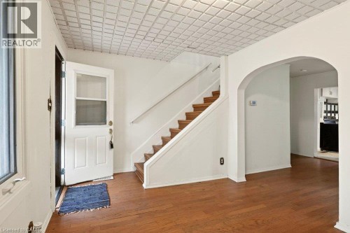 White paneled door with screen, wood-finish flooring, wood staircase with white risers and railing, arched doorway, and white textured ceiling - 23 Frederick Avenue, Hamilton, ON 