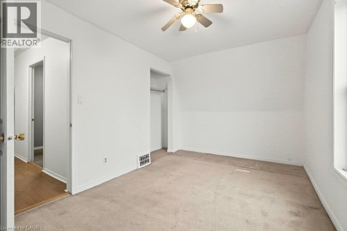 Carpeted room with a ceiling fan light fixture, white walls, and a window - 23 Frederick Avenue, Hamilton, ON 