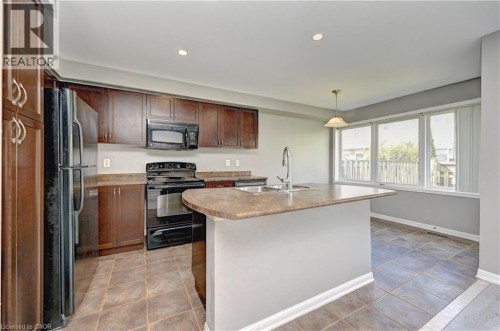 Kitchen featuring dark wood cabinetry, a center island with sink and integrated breakfast bar, black appliances, and tiled flooring - 103 Blackbird Circle, Cambridge, ON 