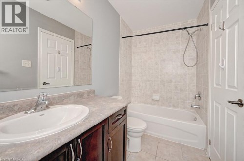 Built-in vanity with a single basin sink, laminate countertop, dark wood-finish cabinetry, tiled shower surround, and tiled flooring - 103 Blackbird Circle, Cambridge, ON 