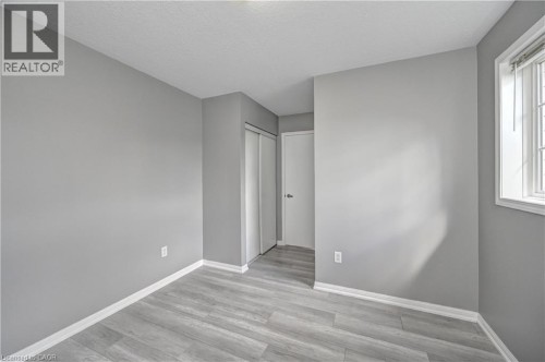 Light gray wood-finish flooring, neutral gray painted walls, white trim, and a white framed window with blinds - 103 Blackbird Circle, Cambridge, ON 