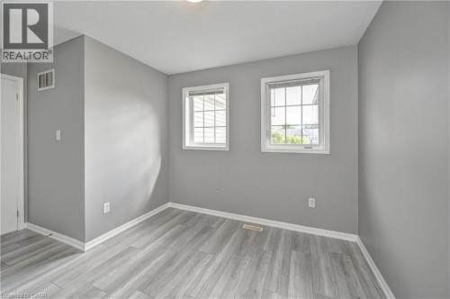 Wood-finish flooring with crisp white trim, two windows with grid detailing, and a flush mount ceiling light - 103 Blackbird Circle, Cambridge, ON 