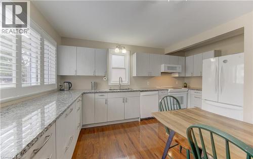 Kitchen featuring white cabinetry, light-toned countertops, wood-finish flooring, and white appliances - 104 Mausser Avenue, Kitchener, ON 