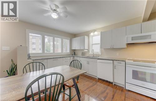 Kitchen featuring wood-finish flooring, white cabinetry, integrated white appliances, and a ceiling fan with light fixture - 104 Mausser Avenue, Kitchener, ON 