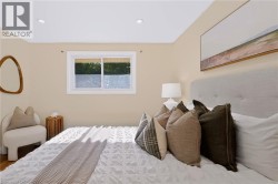Recessed ceiling lighting, light neutral wall paint, wood-finish flooring, sliding window with white trim, upholstered headboard - 