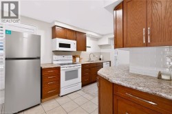 Kitchen featuring wood cabinetry, light-toned countertops, tile flooring, white subway tile backsplash, and stainless steel appliances - 