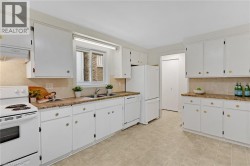 White cabinetry, light-toned tiled flooring, white built-in appliances, and a window above the sink - 