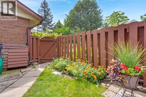Brick exterior with a brown wooden fence and gate, stone-paver walkway, and planted garden bed - 7 Underhill Crescent, Kitchener, ON 