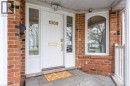 Brick exterior featuring a white paneled entry door with sidelights, an arched window, and a white porch railing - 1389 Lakeshore Road, Burlington, ON 