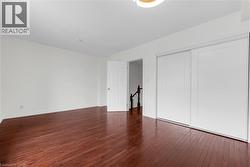 Spacious room featuring rich wood-finish flooring, white walls, and a contemporary ceiling light fixture - 