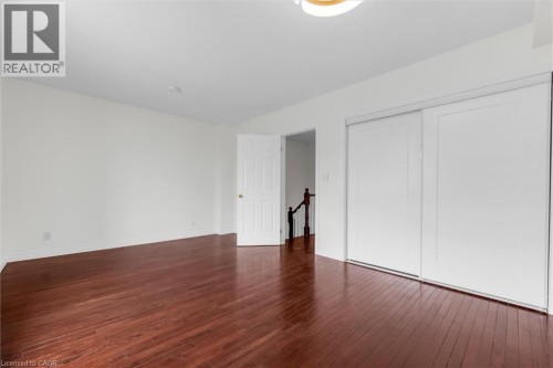Spacious room featuring rich wood-finish flooring, white walls, and a contemporary ceiling light fixture - 1389 Lakeshore Road, Burlington, ON 