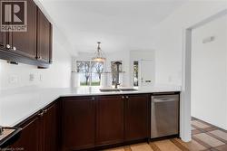 Kitchen featuring dark wood cabinetry, white countertops, stainless steel sink with a gooseneck faucet, and a stainless steel dishwasher - 