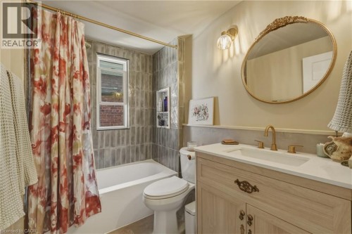 Spa-inspired bathroom featuring a wood-finish vanity with brass hardware, a round brass-framed mirror, and a white ceramic sink - 42 Nightingale Street, Hamilton, ON 