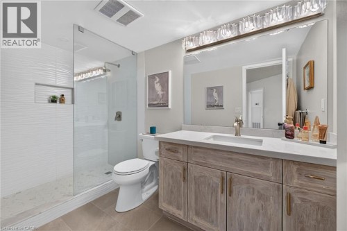 Spacious bathroom featuring a glass-enclosed shower with white textured tile, a built-in shower niche, and a vanity with a light wood-finish double cabinet and a single rectangular undermount sink - 1237 North Shore Boulevard Unit# 405, Burlington, ON 