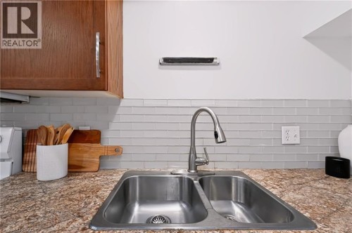Double basin stainless steel sink with a gooseneck faucet, set within a granite-look countertop, complemented by a horizontal stacked tile backsplash and wood-finish cabinetry - 95 Underhill Crescent, Kitchener, ON 