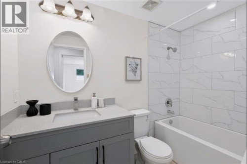Bathroom with a gray vanity, light-toned countertop, oval mirror, and a tiled shower-over-tub combination - 95 Underhill Crescent, Kitchener, ON 
