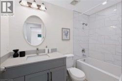 Bathroom with a gray vanity, light-toned countertop, oval mirror, and a tiled shower-over-tub combination - 