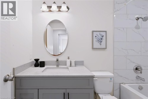 Modern bathroom featuring a gray vanity with ample storage, white quartz countertop, oval mirror with integrated lighting, and tile shower surround with chrome fixtures - 95 Underhill Crescent, Kitchener, ON 