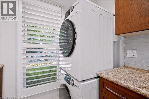 Built-in stacked washer and dryer, wood-finish cabinetry, granite-finish countertop, and light subway tile backsplash - 95 Underhill Crescent, Kitchener, ON 