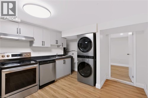 Modern kitchen and laundry space featuring stainless steel appliances, white cabinetry with hardware accents, wood-finish flooring, a dual-stack washer and dryer unit with black finish, and recessed c - 95 Underhill Crescent, Kitchener, ON 