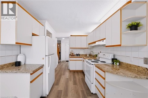 Kitchen featuring ample white cabinetry, wood-finish flooring, white tile backsplash, and granite countertops - 121 University Avenue E Unit# 102, Waterloo, ON 