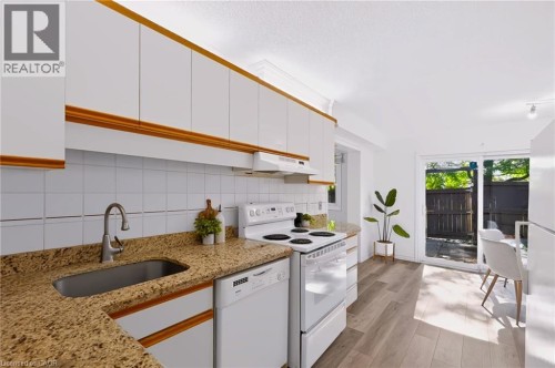 Kitchen featuring white cabinetry with wood trim, granite-style countertops, and a tile backsplash - 121 University Avenue E Unit# 102, Waterloo, ON 