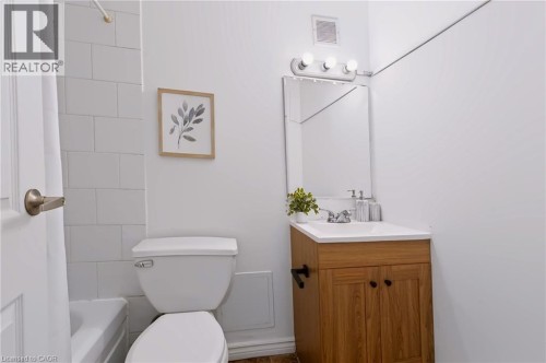 Bathroom with white ceramic tile tub surround, a single vanity with wood-finish cabinetry, and a rectangular mirror with overhead lighting - 121 University Avenue E Unit# 102, Waterloo, ON 