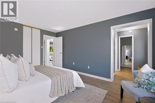 Bedroom featuring wood-finish flooring, a neutral wall color, white trim, and a built-in closet with bi-fold doors - 121 University Avenue E Unit# 102, Waterloo, ON 