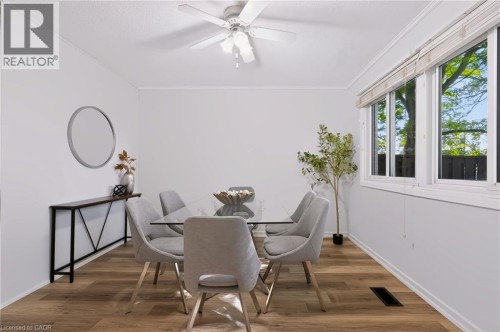 Bright dining space showcasing warm wood-finish flooring, a ceiling fan with integrated lighting, and expansive multi-panel windows flooding the room with natural light - 121 University Avenue E Unit# 102, Waterloo, ON 