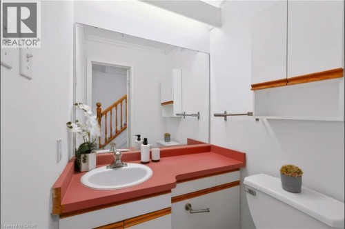 Modern bathroom featuring a distinctive coral-red countertop with integrated circular sink basin, wood-finish trim detailing, and large framed mirror with ample natural lighting from skylight above - 121 University Avenue E Unit# 102, Waterloo, ON 