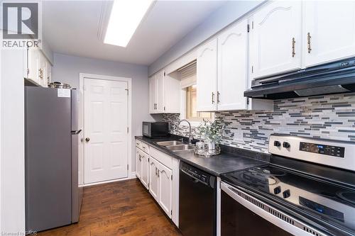 Kitchen featuring white cabinetry with decorative hardware, dark countertops, and a mosaic tile backsplash - 543 Drummerhill Crescent, Waterloo, ON 