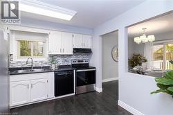 Kitchen featuring white cabinetry, dark countertops, a mosaic tile backsplash, stainless steel appliances, and dark wood-finish flooring - 