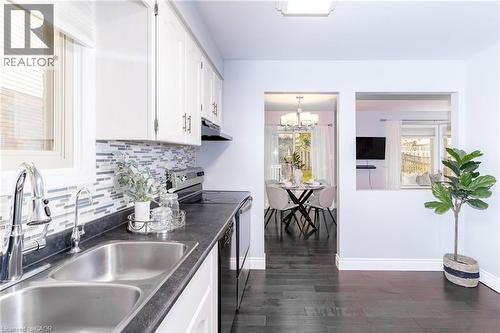 Kitchen featuring a double stainless steel sink, mosaic tile backsplash, white cabinetry, and dark countertops - 543 Drummerhill Crescent, Waterloo, ON 