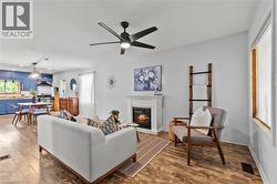Open-concept living space featuring wood-finish flooring, a contemporary ceiling fan with integrated lighting, and a white mantel fireplace - 