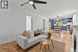 Expansive open-concept living area featuring wood-finish flooring, a modern black ceiling fan with integrated lighting, and a white mantelpiece - 