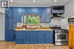 Kitchen featuring blue cabinetry, wood-finish flooring, butcher block countertops, white subway tile backsplash, and stainless steel appliances - 