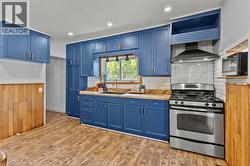Kitchen featuring blue cabinetry, wood-finish countertops, subway tile backsplash, stainless steel gas range with range hood, and wood-finish flooring - 