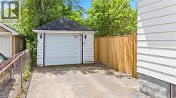 Detached garage with a paneled door, exterior wall sconces, asphalt shingle roof, and a wood privacy fence - 