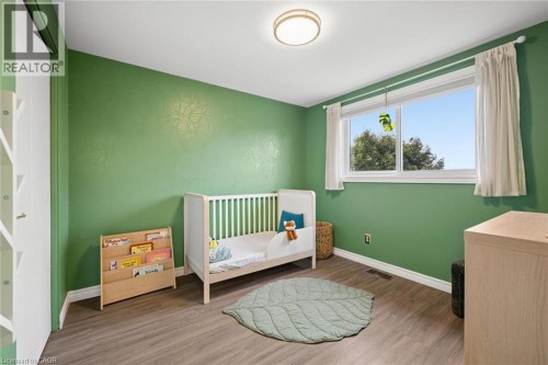 Wood-finish flooring, accent wall with a subtle pattern, and a window with white trim - 76 Cluthe Crescent, Kitchener, ON 