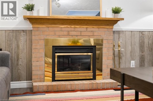 Brick fireplace with a brass-trimmed insert, wood mantel, and wood-panel accent wall - 76 Cluthe Crescent, Kitchener, ON 