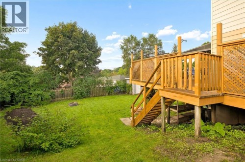 Spacious backyard featuring a manicured lawn, an elevated wood deck with stairs, a wood privacy fence, and mature trees - 76 Cluthe Crescent, Kitchener, ON 